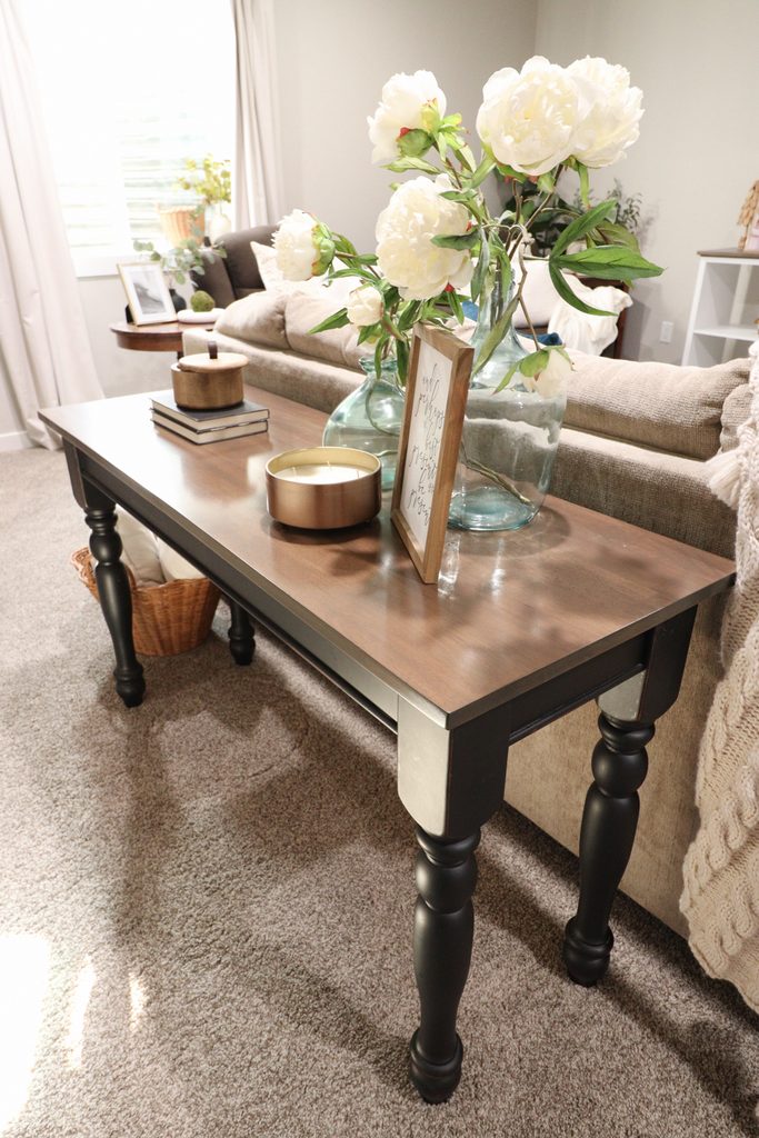 Wooden console table with vases of white flowers, candle, books, and framed sign in a cozy living room.
