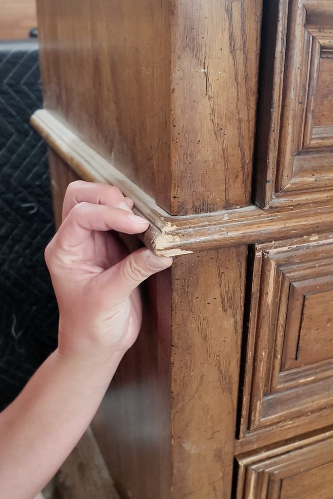 Hand pointing to a chip in the wooden molding of a dresser.