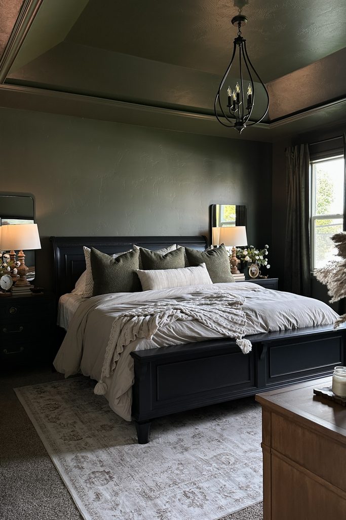 A dark green color drenched bedroom featuring a black bed frame with neutral bedding and a dark metal chandelier.