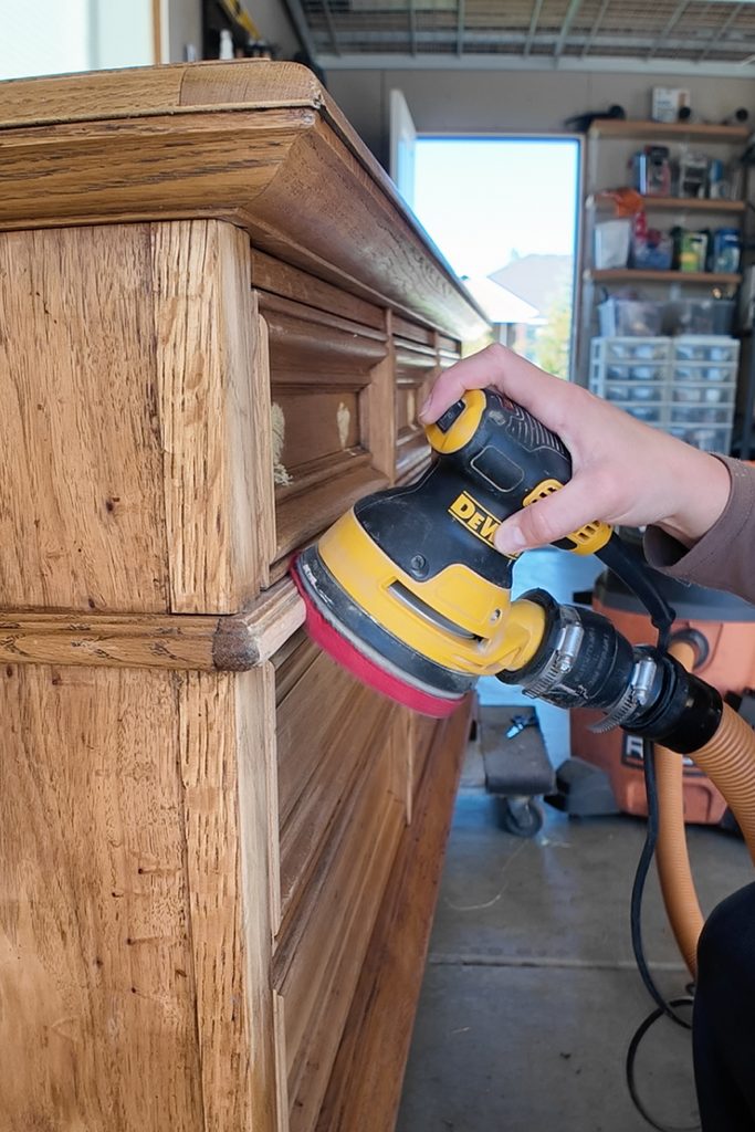 Hand sanding the side of a wooden dresser with a DeWalt orbital sander and foam pad