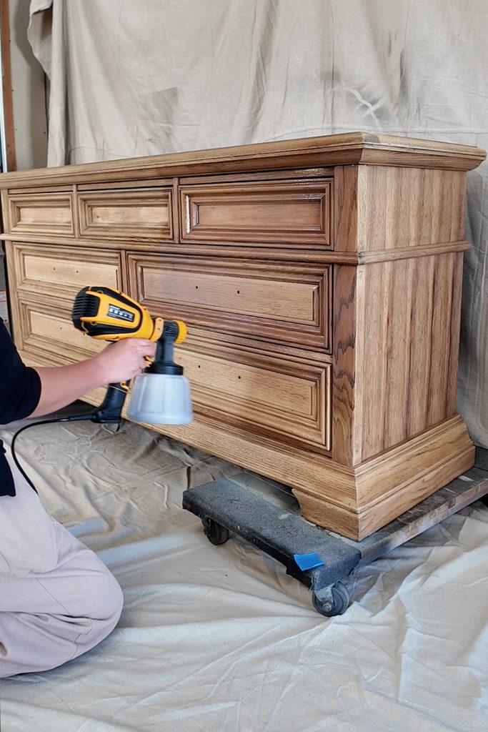 Person using a handheld paint sprayer on a wooden dresser.