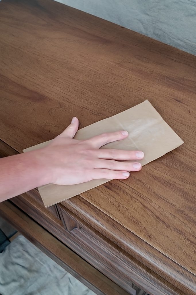 A hand holding a piece of brown paper bag against a wooden surface.